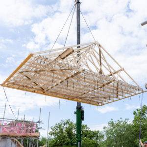 A timber frame being lifted by a crane to be placed as part of a housing development