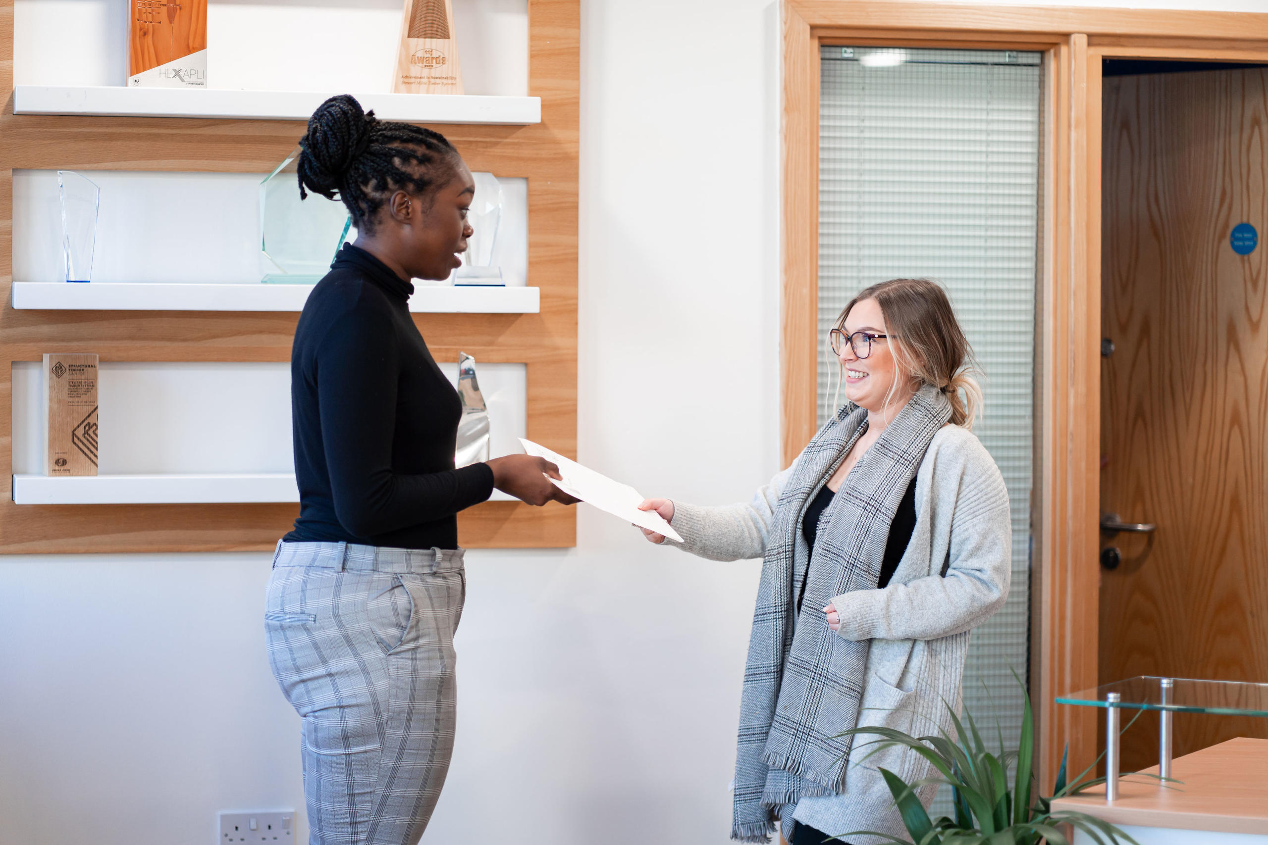 Two women employees of James Donaldson Group discussing and handing over a bit of paper to one another