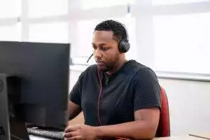 A member of the James Donaldson Group sitting at his desk with a headset on, looking at a monitor