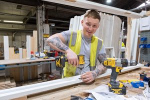 A male employee of Rowan building a frame and smiling towards the camera